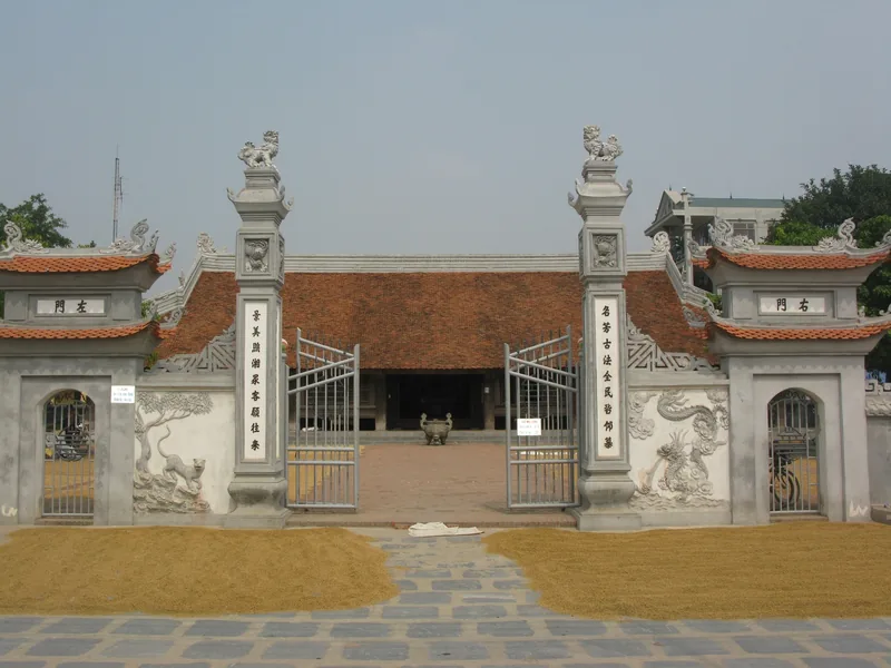 Cổng đá và sân đình Đình Bảng ở Bắc Ninh, với thóc đang được phơi trên nền sân bên ngoài.