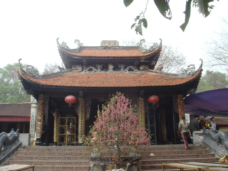 Ngôi đền mái ngói cong truyền thống với đèn lồng đỏ và cây hoa đào tại Đền Bà Chúa Kho, Bắc Ninh.